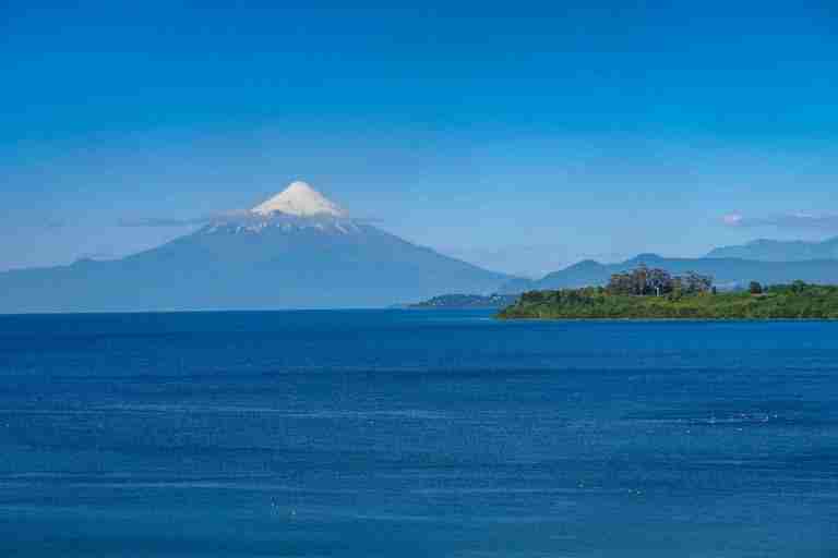 Breathtaking view of Osorno Volcano towering over Lake Llanquihue under a clear blue sky.